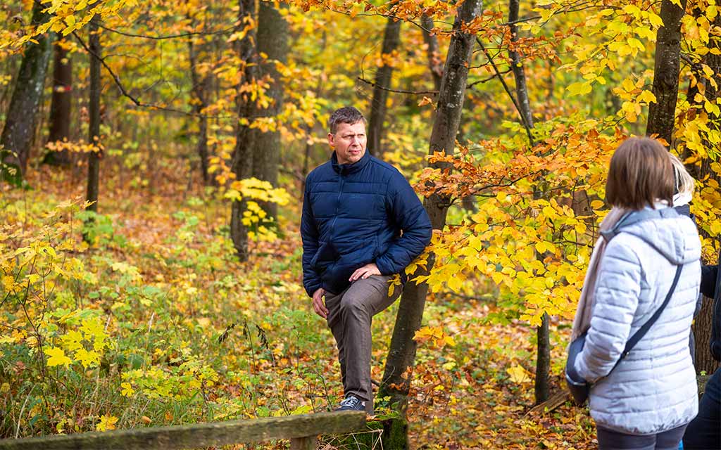 Ein Mann mit einer blauen Winterjacke steht im Wald und spricht mit anderen Menschen.