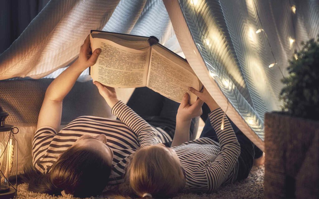 Zwei Personen lesen ein Buch unter einem Zelt in einem Zimmer