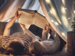 Zwei Personen lesen ein Buch unter einem Zelt in einem Zimmer