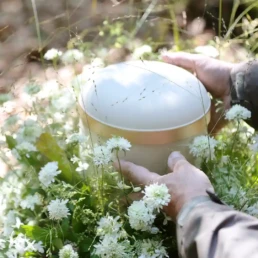 hände an einer weißen urne mit blumen geschmückt